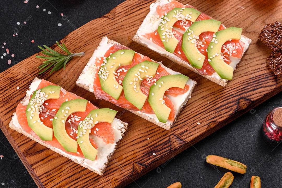 Delicioso sanduíche fresco com peixe vermelho, manteiga, pão e abacate em uma mesa de concreto escuro