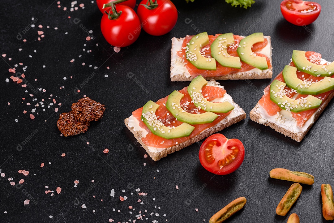 Delicioso sanduíche fresco com peixe vermelho, manteiga, pão e abacate em uma mesa de concreto escuro