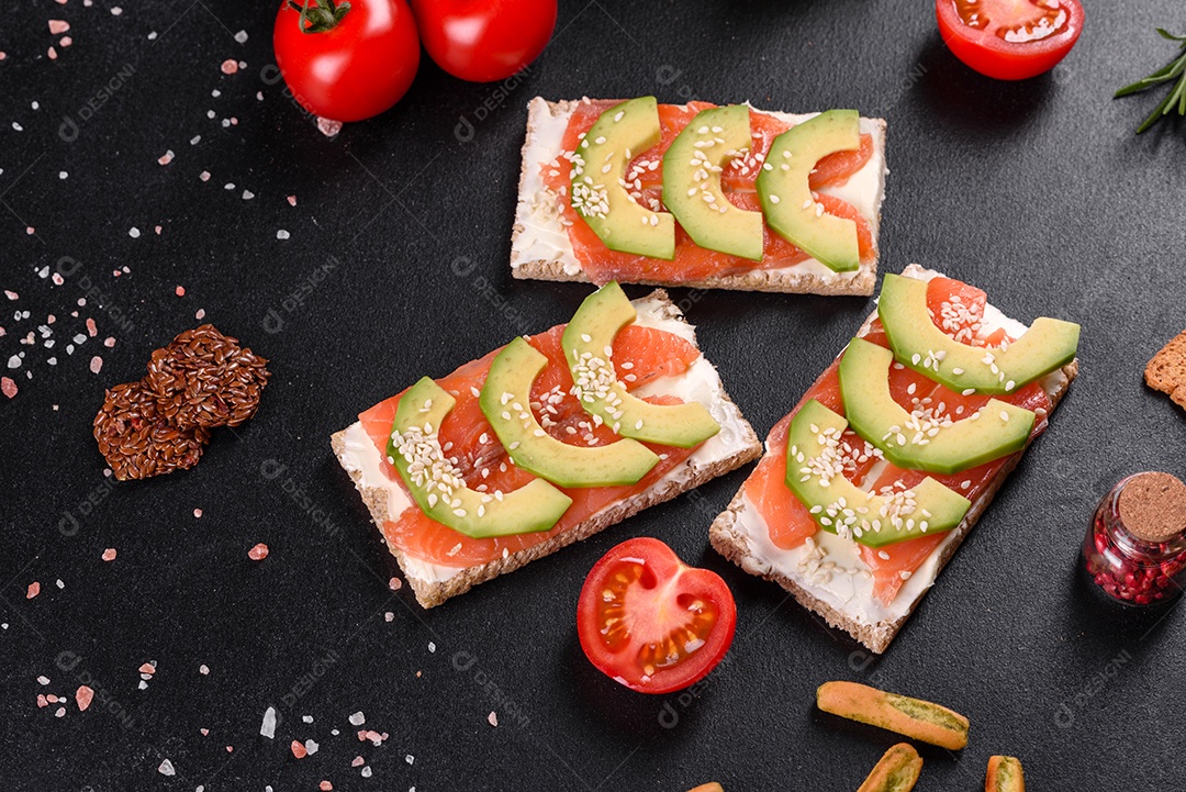 Delicioso sanduíche fresco com peixe vermelho, manteiga, pão e abacate em uma mesa de concreto escuro