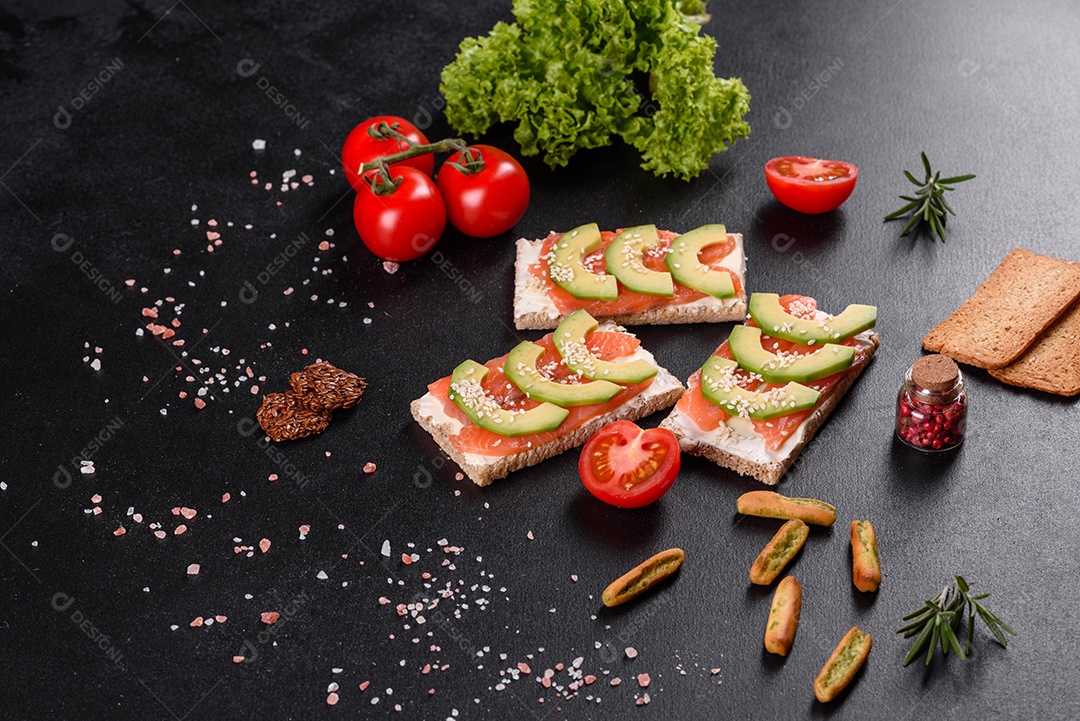 Delicioso sanduíche fresco com peixe vermelho, manteiga, pão e abacate em uma mesa de concreto escuro
