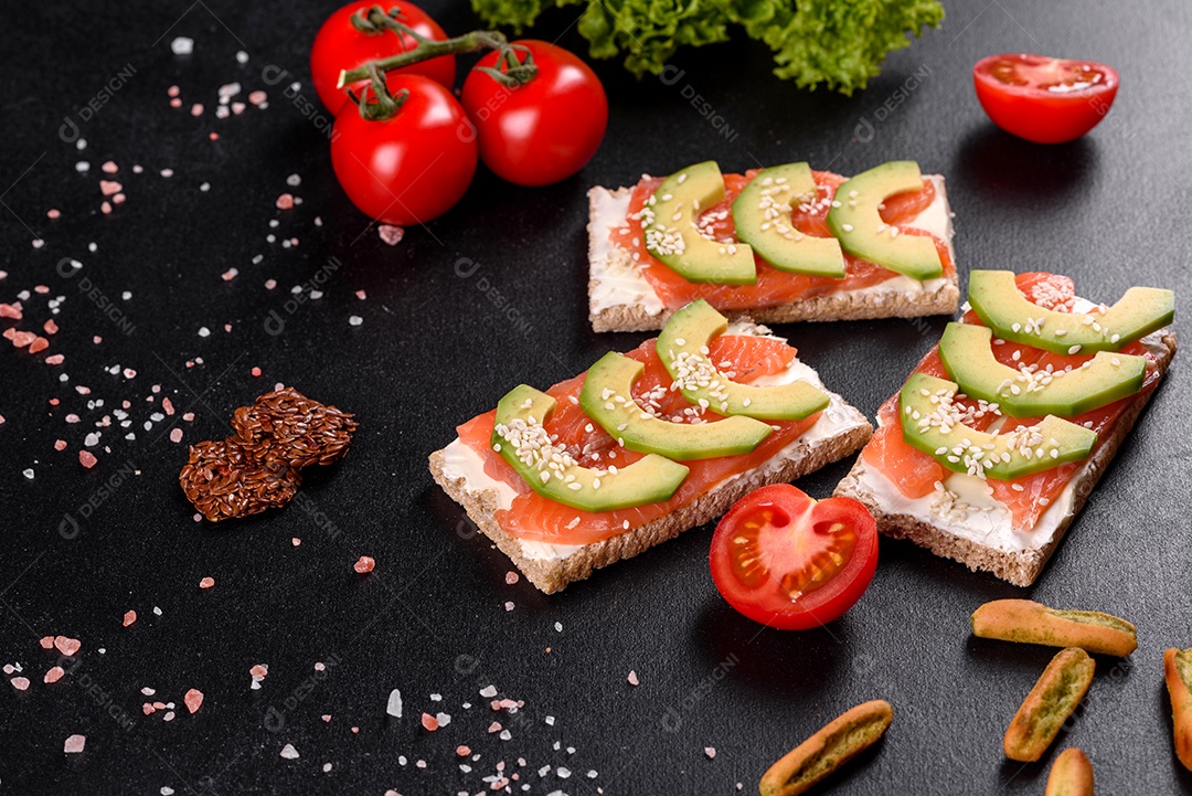 Delicioso sanduíche fresco com peixe vermelho, manteiga, pão e abacate em uma mesa de concreto escuro