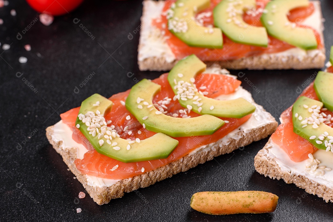 Delicioso sanduíche fresco com peixe vermelho, manteiga, pão e abacate em uma mesa de concreto escuro