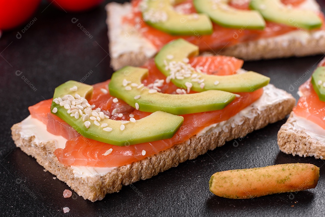 Delicioso sanduíche fresco com peixe vermelho, manteiga, pão e abacate em uma mesa de concreto escuro