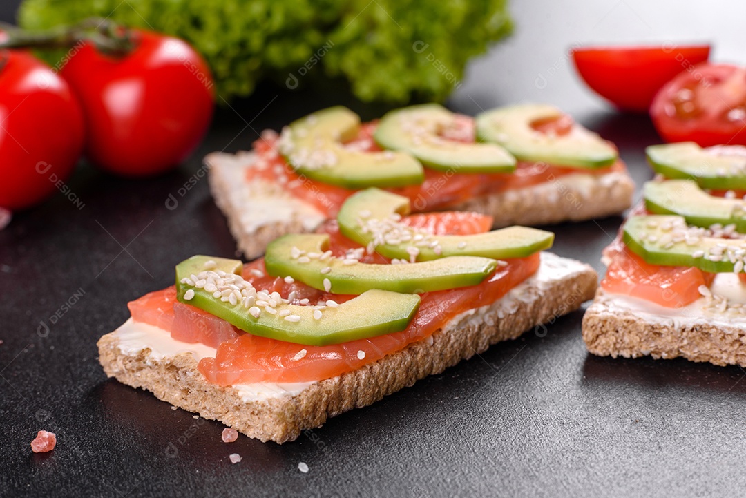 Delicioso sanduíche fresco com peixe vermelho, manteiga, pão e abacate em uma mesa de concreto escuro