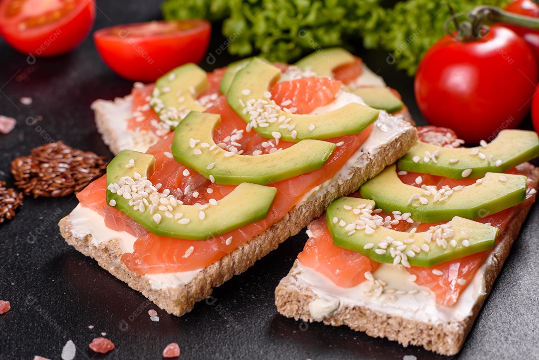 Delicioso sanduíche fresco com peixe vermelho, manteiga, pão e abacate em uma mesa de concreto escuro