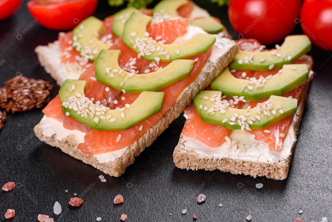 Delicioso sanduíche fresco com peixe vermelho, manteiga, pão e abacate em uma mesa de concreto escuro