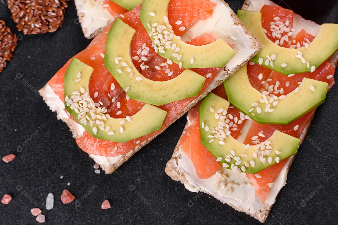 Delicioso sanduíche fresco com peixe vermelho, manteiga, pão e abacate em uma mesa de concreto escuro