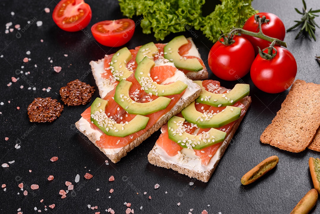 Delicioso sanduíche fresco com peixe vermelho, manteiga, pão e abacate em uma mesa de concreto escuro