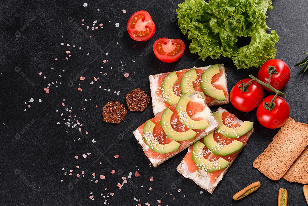 Delicioso sanduíche fresco com peixe vermelho, manteiga, pão e abacate em uma mesa de concreto escuro