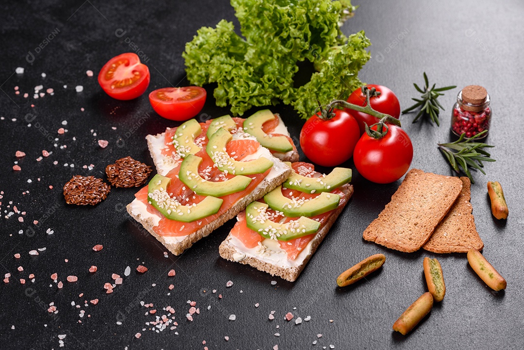 Delicioso sanduíche fresco com peixe vermelho, manteiga, pão e abacate em uma mesa de concreto escuro