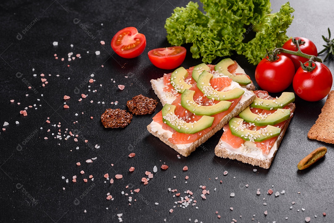 Delicioso sanduíche fresco com peixe vermelho, manteiga, pão e abacate em uma mesa de concreto escuro