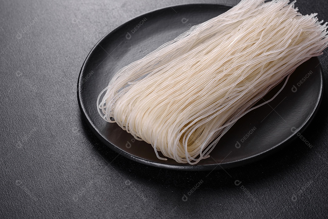 Macarrão de arroz saboroso com tomate, pimenta vermelha, cogumelos e frutos do mar em um fundo escuro de concreto