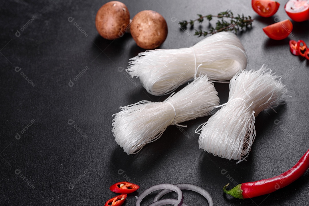 Macarrão de arroz saboroso com tomate, pimenta vermelha, cogumelos e frutos do mar em um fundo escuro de concreto