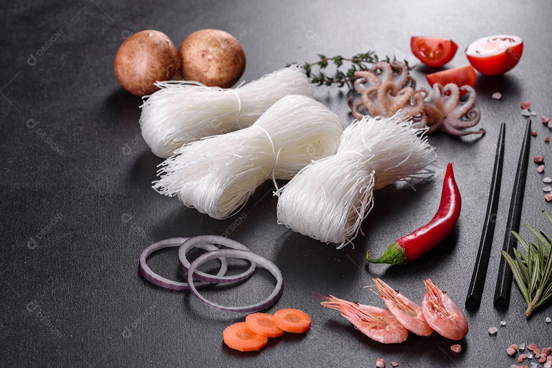 Macarrão de arroz saboroso com tomate, pimenta vermelha, cogumelos e frutos do mar em um fundo escuro de concreto
