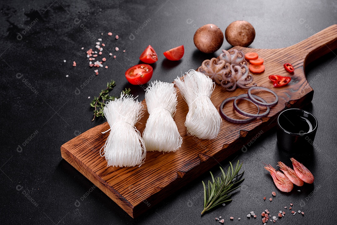 Macarrão de arroz saboroso com tomate, pimenta vermelha, cogumelos e frutos do mar em um fundo escuro de concreto