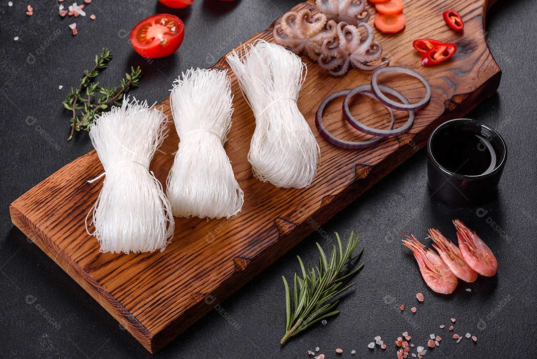Macarrão de arroz saboroso com tomate, pimenta vermelha, cogumelos e frutos do mar em um fundo escuro de concreto