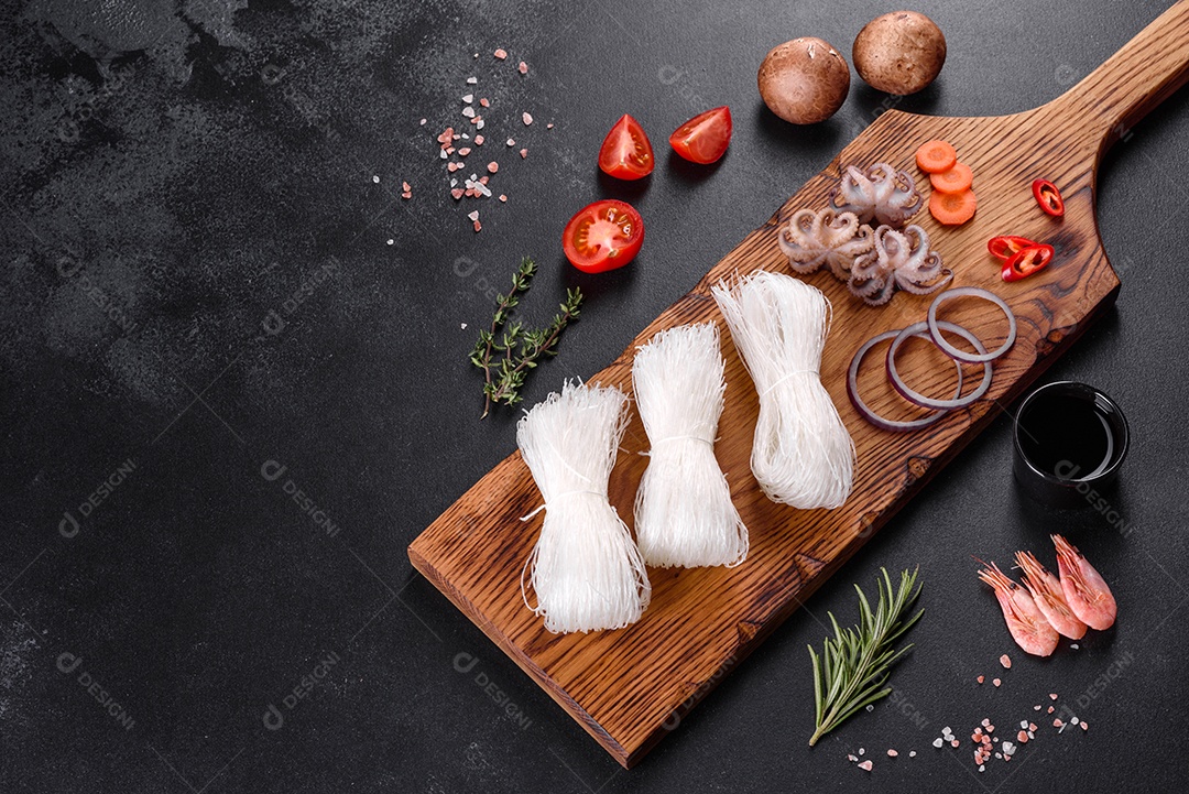 Macarrão de arroz saboroso com tomate, pimenta vermelha, cogumelos e frutos do mar em um fundo escuro de concreto