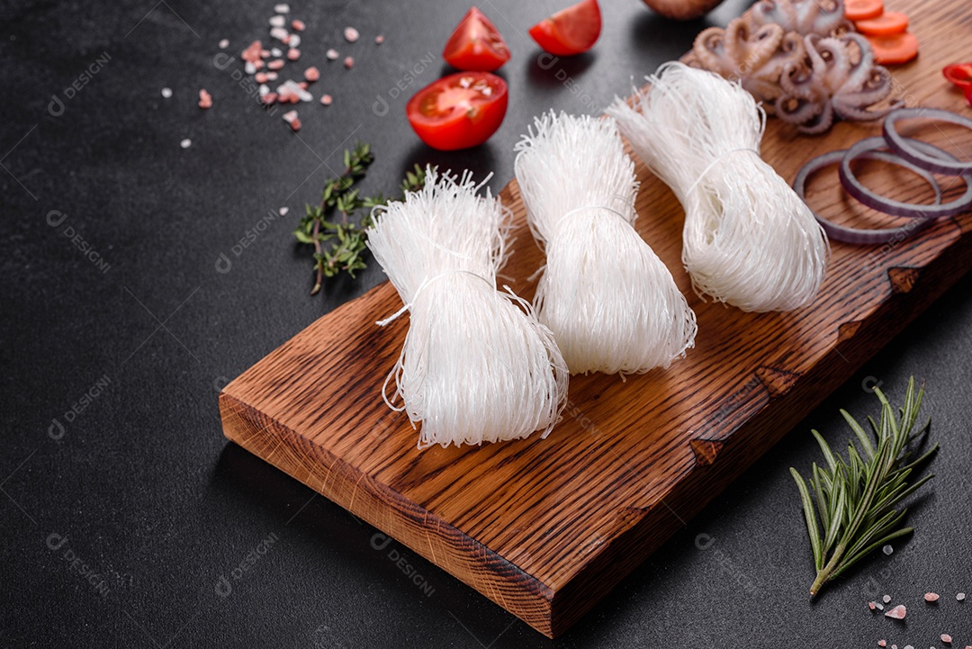 Macarrão de arroz saboroso com tomate, pimenta vermelha, cogumelos e frutos do mar em um fundo escuro de concreto