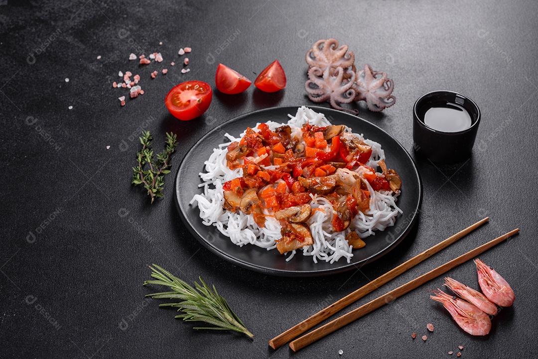 Macarrão de arroz saboroso com tomate, pimenta vermelha, cogumelos e frutos do mar em um fundo escuro de concreto