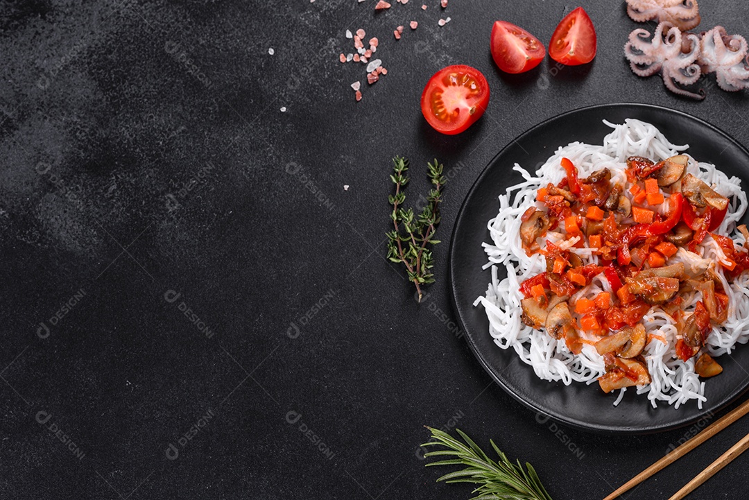 Macarrão de arroz saboroso com tomate, pimenta vermelha, cogumelos e frutos do mar em um fundo escuro de concreto