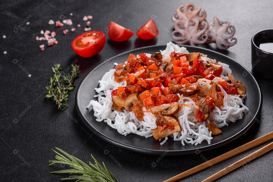 Macarrão de arroz saboroso com tomate, pimenta vermelha, cogumelos e frutos do mar em um fundo escuro de concreto