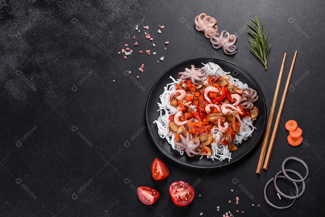 Macarrão de arroz saboroso com tomate, pimenta vermelha, cogumelos e frutos do mar em um fundo escuro de concreto