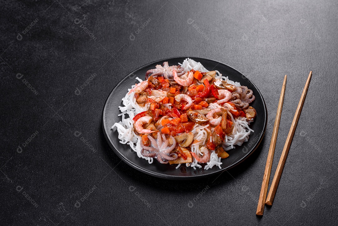 Macarrão de arroz saboroso com tomate, pimenta vermelha, cogumelos e frutos do mar em um fundo escuro de concreto