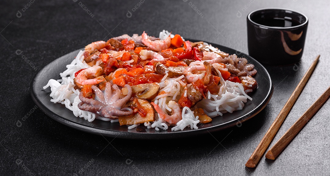 Macarrão de arroz saboroso com tomate, pimenta vermelha, cogumelos e frutos do mar em um fundo escuro de concreto