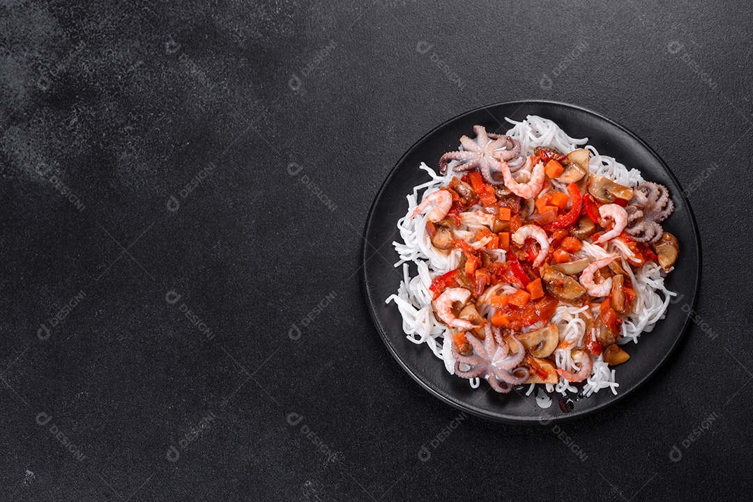 Macarrão de arroz saboroso com tomate, pimenta vermelha, cogumelos e frutos do mar em um fundo escuro de concreto
