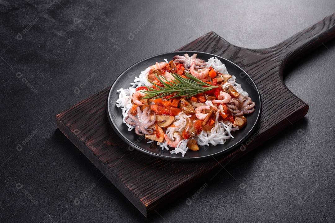 Macarrão de arroz saboroso com tomate, pimenta vermelha, cogumelos e frutos do mar em um fundo escuro de concreto