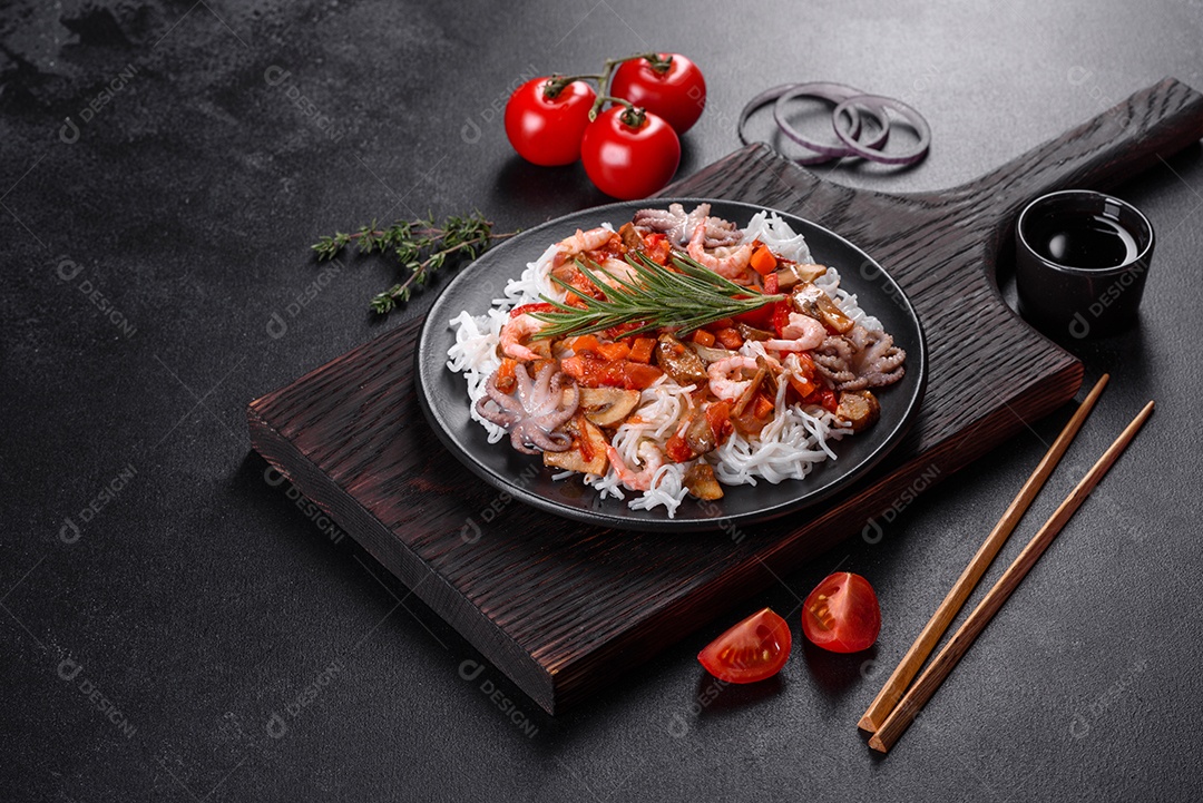 Macarrão de arroz saboroso com tomate, pimenta vermelha, cogumelos e frutos do mar em um fundo escuro de concreto