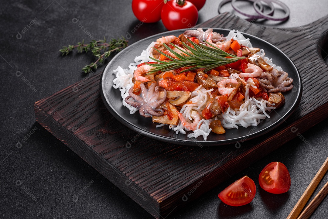 Macarrão de arroz saboroso com tomate, pimenta vermelha, cogumelos e frutos do mar em um fundo escuro de concreto