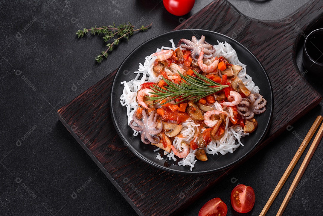 Macarrão de arroz saboroso com tomate, pimenta vermelha, cogumelos e frutos do mar em um fundo escuro de concreto