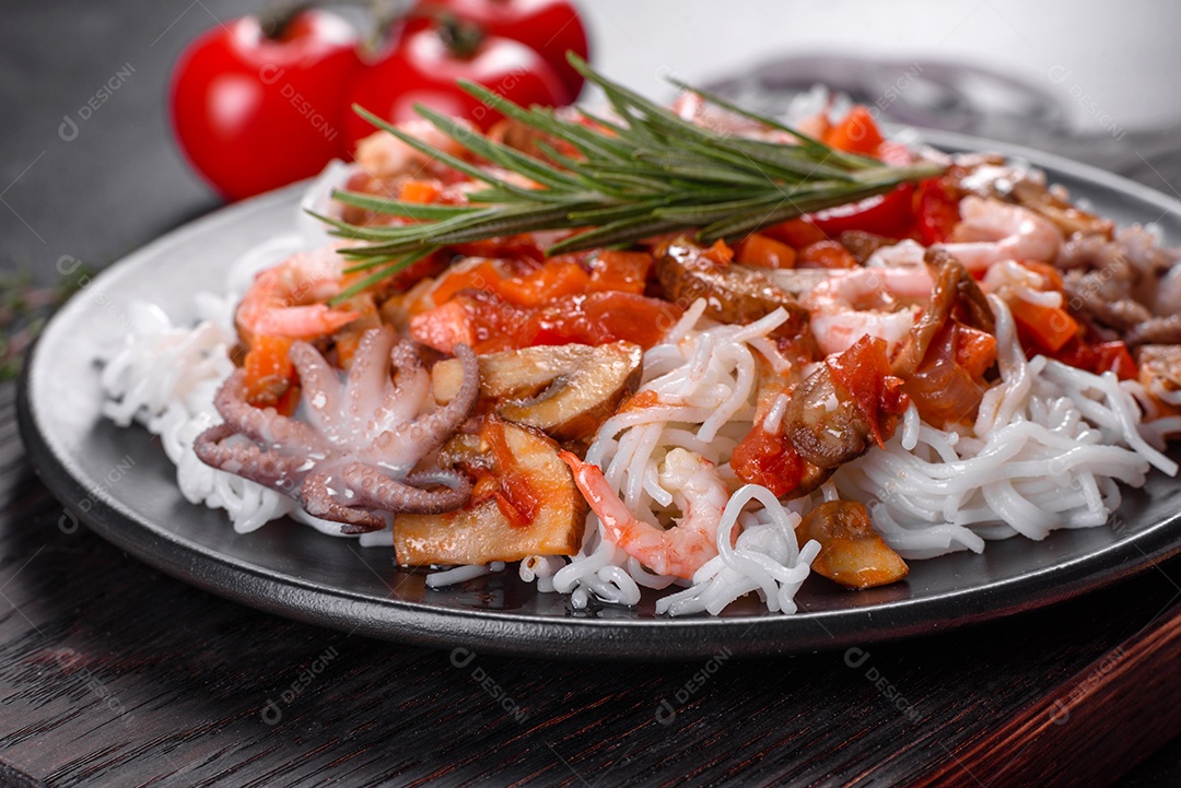 Macarrão de arroz saboroso com tomate, pimenta vermelha, cogumelos e frutos do mar em um fundo escuro de concreto