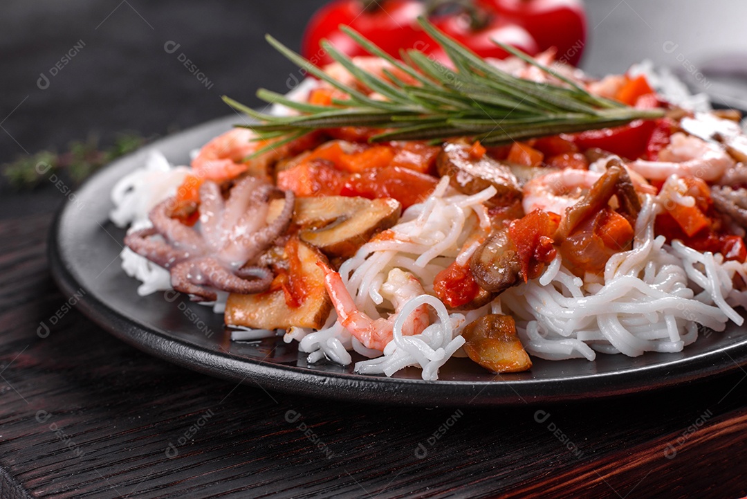 Macarrão de arroz saboroso com tomate, pimenta vermelha, cogumelos e frutos do mar em um fundo escuro de concreto