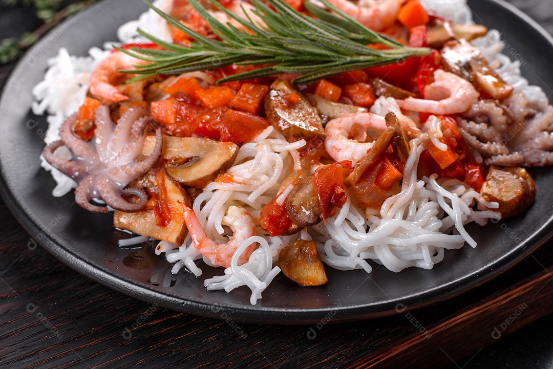 Macarrão de arroz saboroso com tomate, pimenta vermelha, cogumelos e frutos do mar em um fundo escuro de concreto