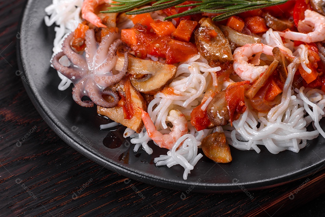 Macarrão de arroz saboroso com tomate, pimenta vermelha, cogumelos e frutos do mar em um fundo escuro de concreto