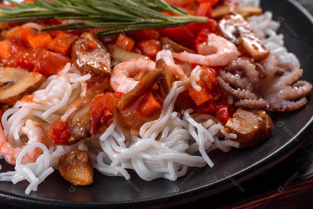 Macarrão de arroz saboroso com tomate, pimenta vermelha, cogumelos e frutos do mar em um fundo escuro de concreto