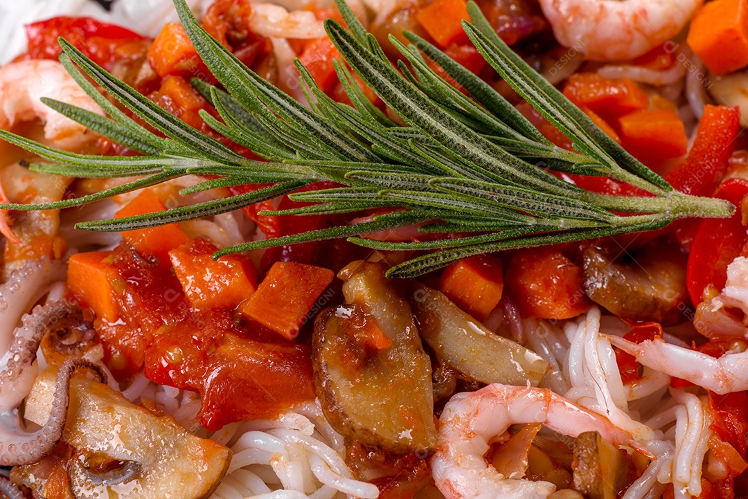 Macarrão de arroz saboroso com tomate, pimenta vermelha, cogumelos e frutos do mar em um fundo escuro de concreto