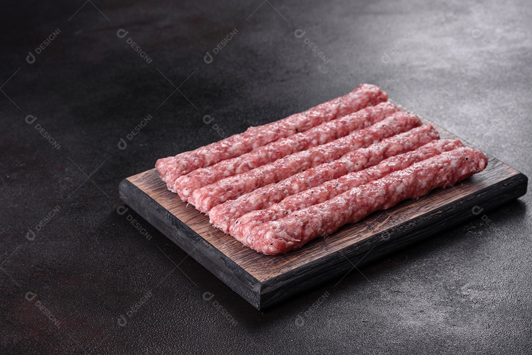 Salsichas de porco cruas frescas com especiarias numa tábua de madeira sobre uma mesa de concreto escuro