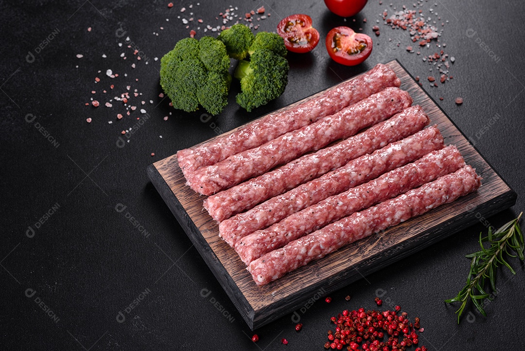 Salsichas de porco cruas frescas com especiarias numa tábua de madeira sobre uma mesa de concreto escuro