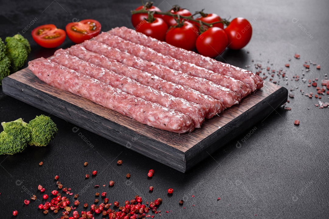 Salsichas de porco cruas frescas com especiarias numa tábua de madeira sobre uma mesa de concreto escuro