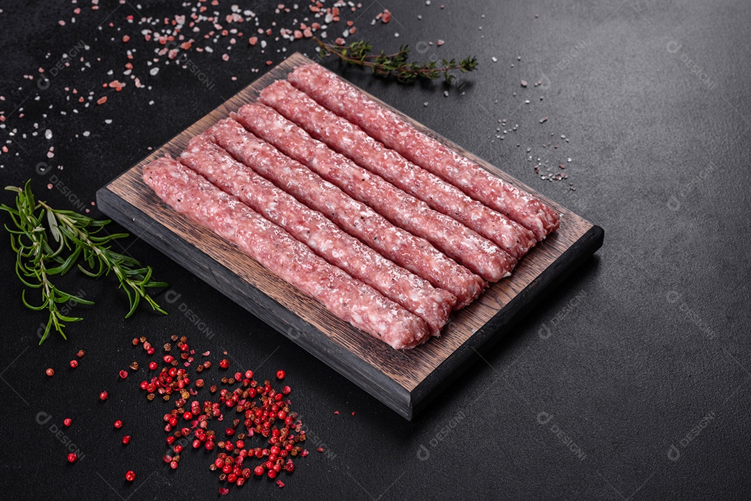 Salsichas de porco cruas frescas com especiarias numa tábua de madeira sobre uma mesa de concreto escuro