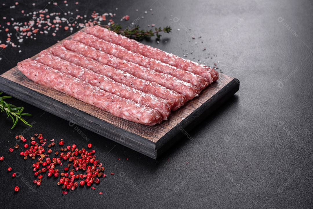 Salsichas de porco cruas frescas com especiarias numa tábua de madeira sobre uma mesa de concreto escuro