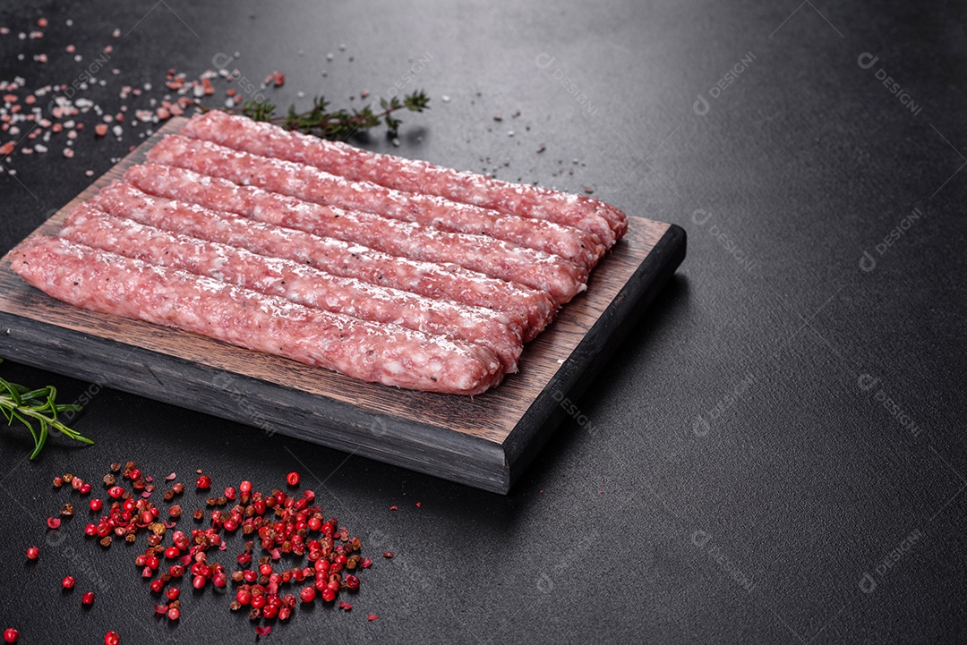 Salsichas de porco cruas frescas com especiarias numa tábua de madeira sobre uma mesa de concreto escuro