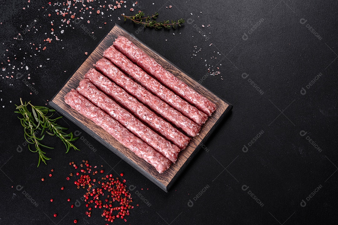 Salsichas de porco cruas frescas com especiarias numa tábua de madeira sobre uma mesa de concreto escuro