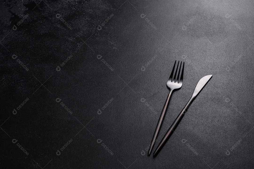 Talheres pretos sobre uma mesa escura de concreto. Preparação da mesa de jantar