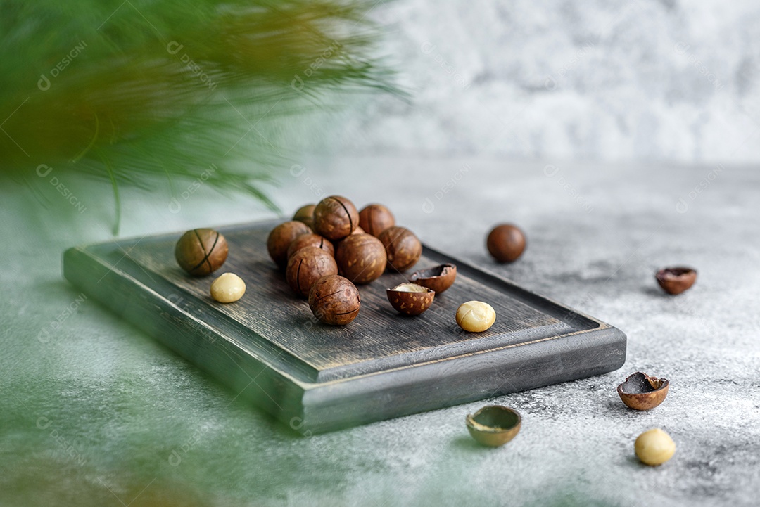 Vários tipos de nozes contra o fundo de ramos de abeto numa tábua de madeira sobre um fundo de concreto claro