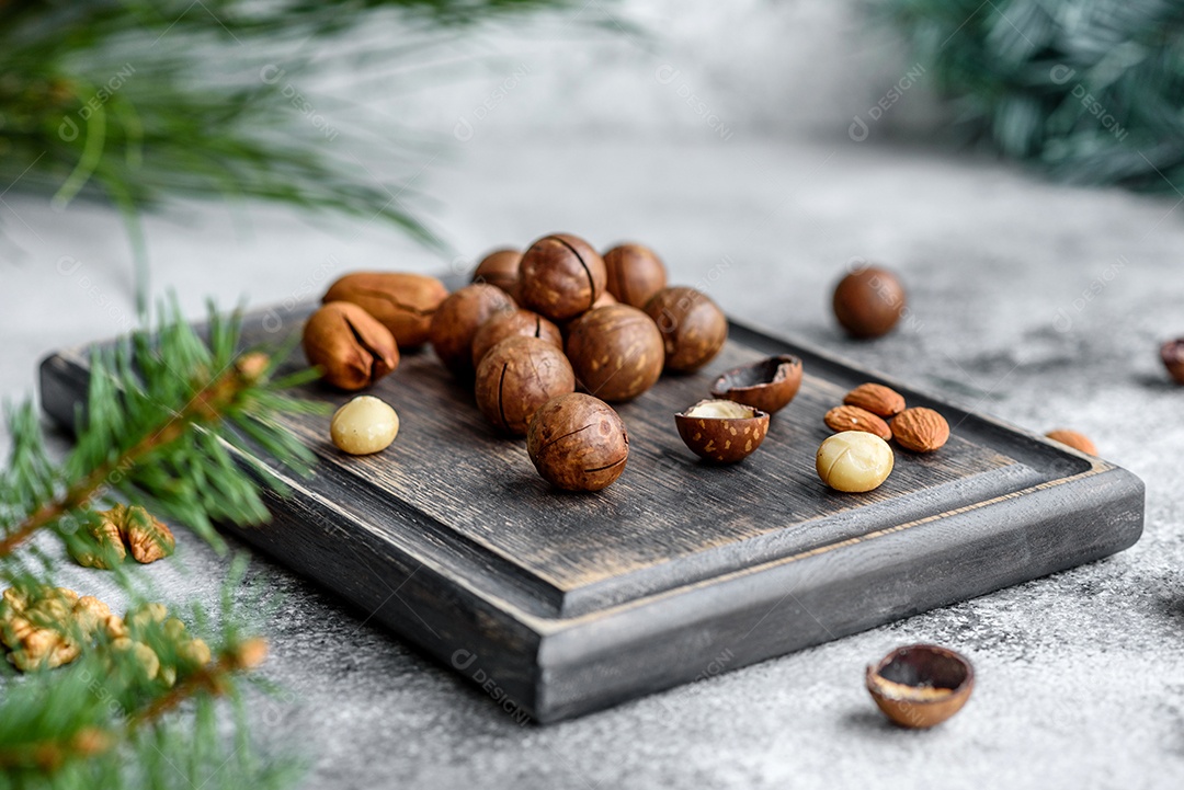 Vários tipos de nozes contra o fundo de ramos de abeto numa tábua de madeira sobre um fundo de concreto claro