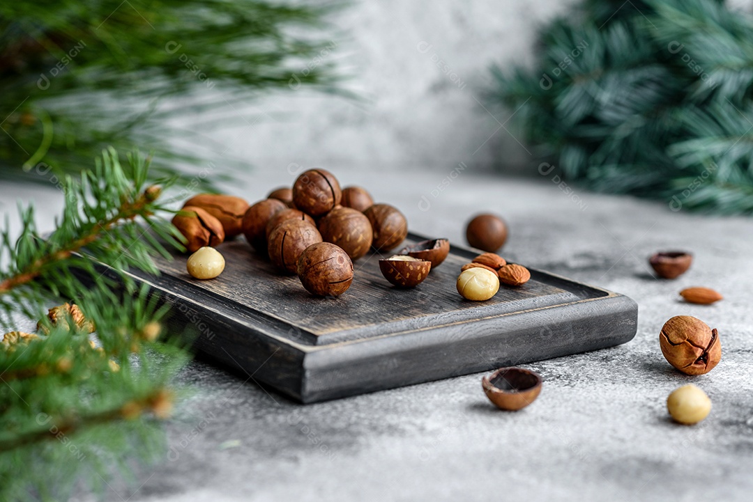Vários tipos de nozes contra o fundo de ramos de abeto numa tábua de madeira sobre um fundo de concreto claro